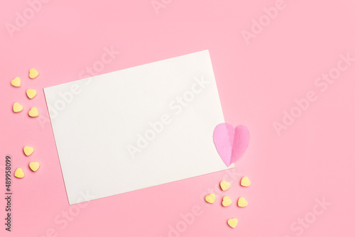 Un sobre blanco junto a un corazón rosa y corazones pequeños amarillos sobre un fondo rosa pastel liso y aislado. Vista superior. Copy space © Mercedes Fittipaldi