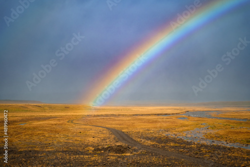 Icelandic nature landscape. Rainbow after rain, road and river. West Iceland region