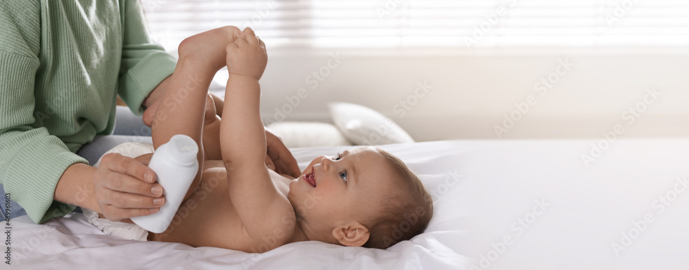 Mother with bottle of dusting powder near her cute baby at home. Banner ...