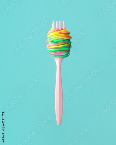 Creative food concept. Minimalistic composition with fork and fun spaghetti on mint background. Eating tasty colorful pasta dish idea.