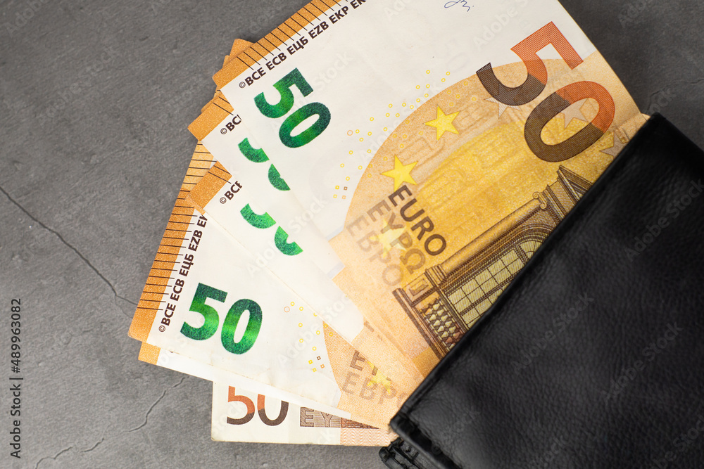 Black wallet full of money - 50 euro banknotes on gray background.
