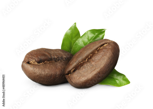Aromatic roasted coffee beans and fresh green leaves on white background