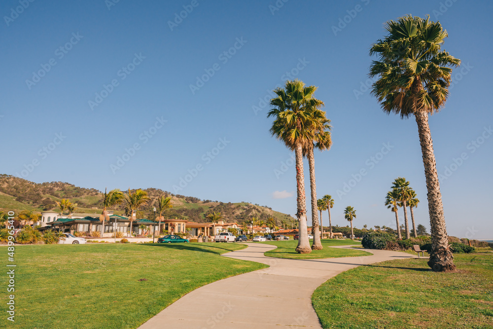 Long walkway along the shore, houses with nicelylandscaped front the yard and clear blue sky on background in a small beach town, California
