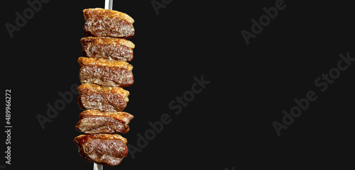 Picanha. Brazilian traditional steak in barbecue. Slices of grilled Picanha on a spit. Black background photo