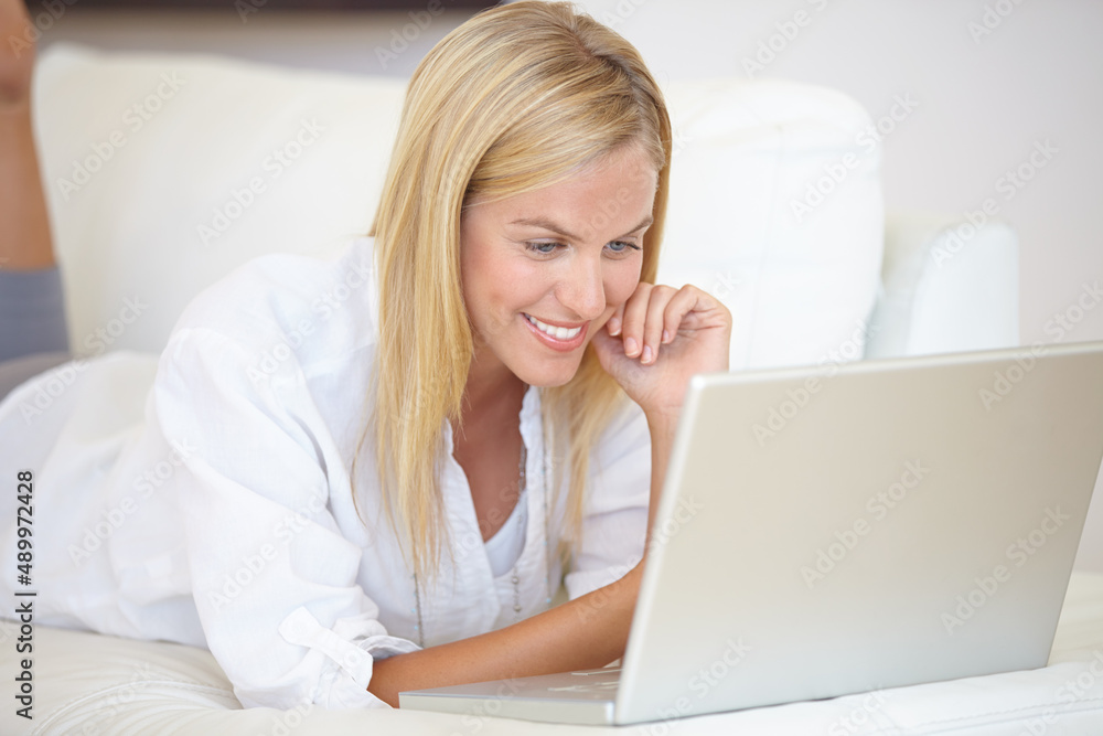 Getting the latest news online. A gorgeous young woman working on her laptop while lying on the sofa. Getting the latest news online. A gorgeous young woman working on her laptop while lying on the sofa.