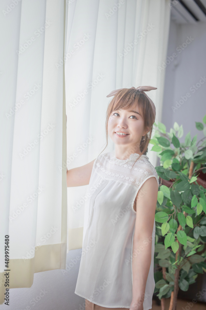 Fototapeta premium 白いカーテンから差し込む朝日を浴びる若い女性 