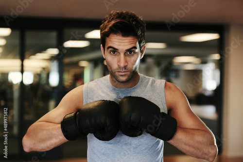 Fiercely focused competitor. Portrait of a focused man wearing boxing gloves and sport clothing posing ready to fight at the gym.