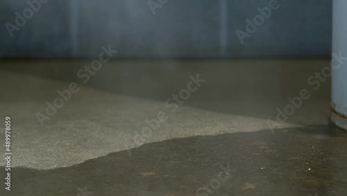 A slider shot of an electric water heater leaking from the access panel and steam from the hot water rises from the concrete floor of a basement with a cinder block wall in the background. photo