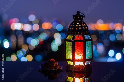 Lantern and small plate of dates fruit with city bokeh light background for the Muslim feast of the holy month of Ramadan Kareem.