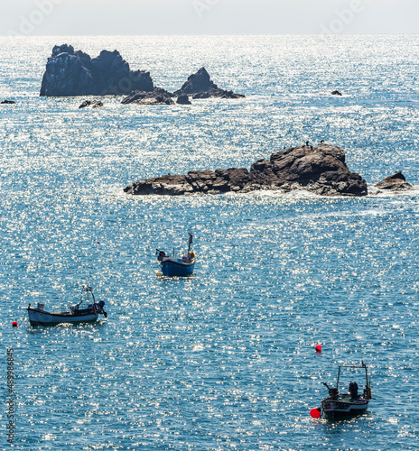 Cornish fishing boats and pinnacles of rock backlit by summer sunlight, protruding from the sea beyond Lizard Point,southern Cornwall, England, United Kingdom. photo