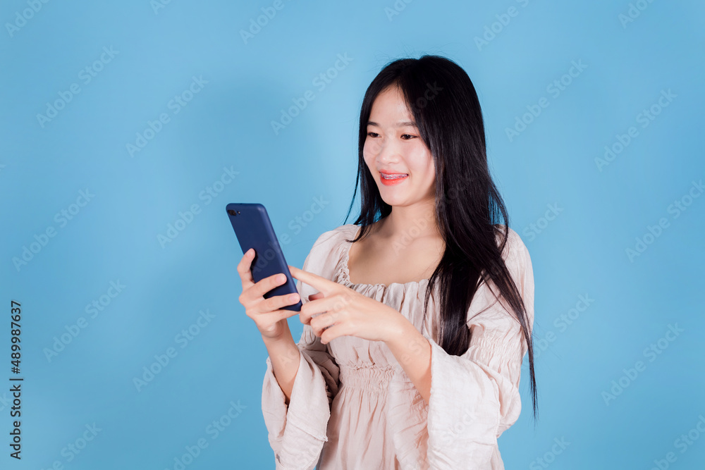 Portrait of smiling asian woman using a smartphone on blue background Portrait of smiling asian woman using a smartphone on blue background