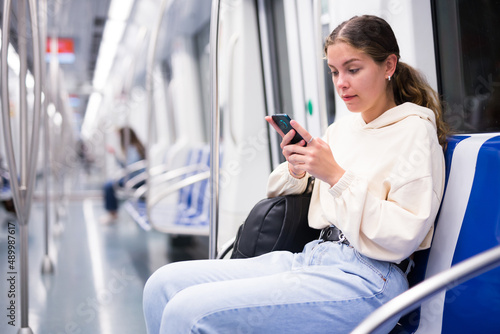 Young woman train passenger using mobile phone during travel in underground train carriage