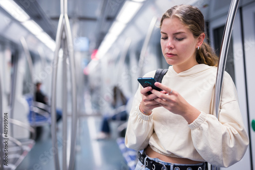Focused girl riding on a subway train is texting with friends on her mobile phone