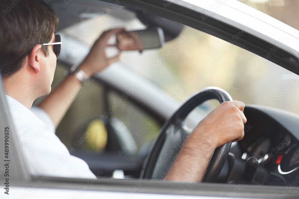 Seeing the road behind him. A man adjusting his rear view mirror while driving.