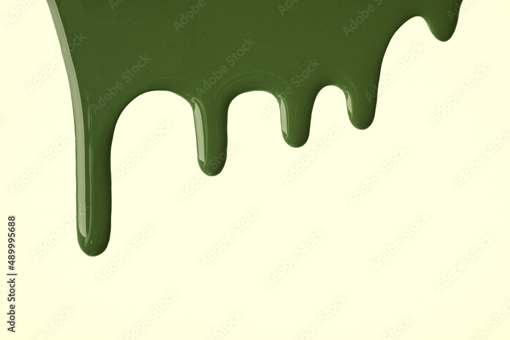 Dark green liquid drops of paint color flow down on light olive background. Abstract khaki backdrop