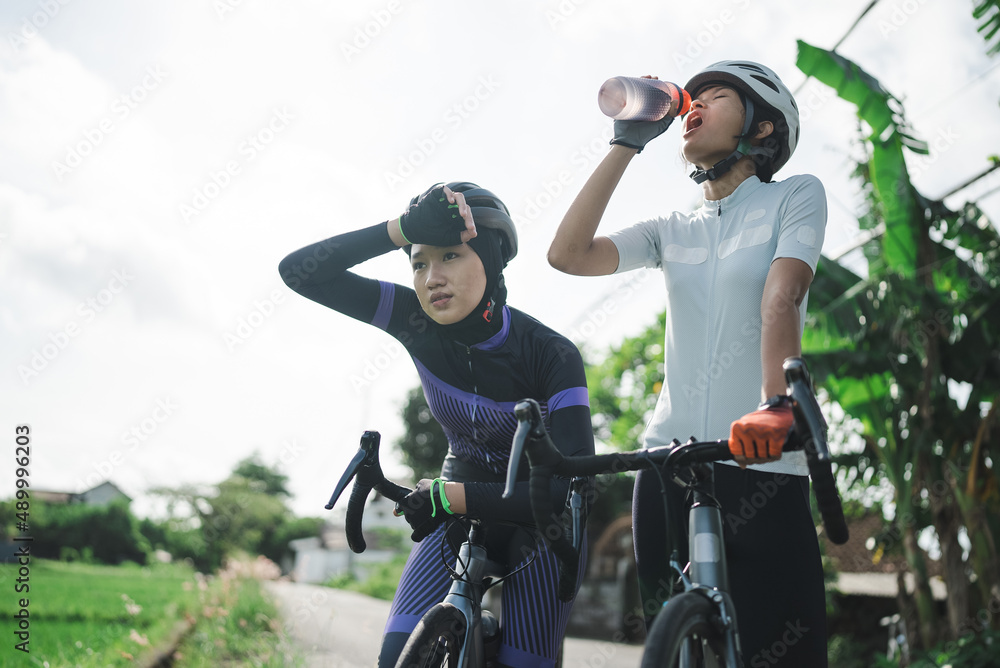 female cyclist having a bottle of water on the road side