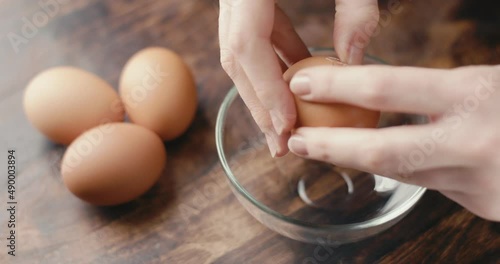Female hand breaks egg in glass bowl kitchen close up in slow motion