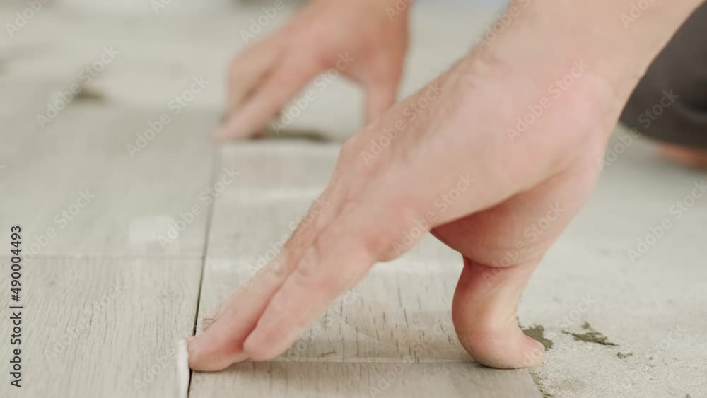 Laying floor ceramic tile. Renovating the floor. Construction workers installing ceramic floor over concrete floor using tile levelers, trowels and tile mortar. Close up, selective focus Laying floor ceramic tile. Renovating the floor. Construction workers installing ceramic floor over concrete floor using tile levelers, trowels and tile mortar. Close up, selective focus