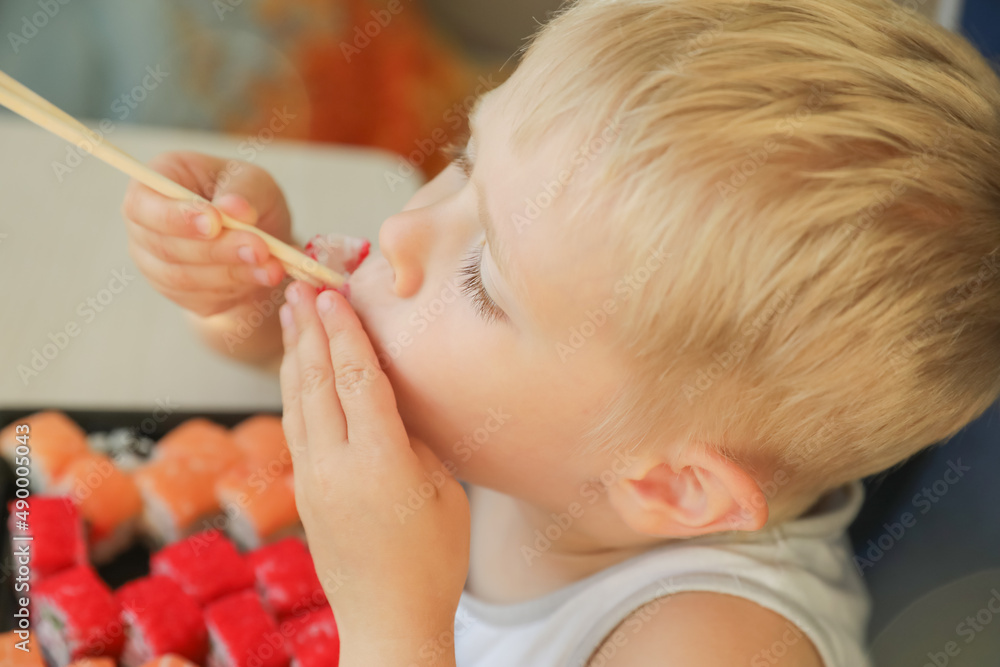 The child is eating sushi. Boy learning to eat rolls with chopsticks. The child is eating sushi. Boy learning to eat rolls with chopsticks.