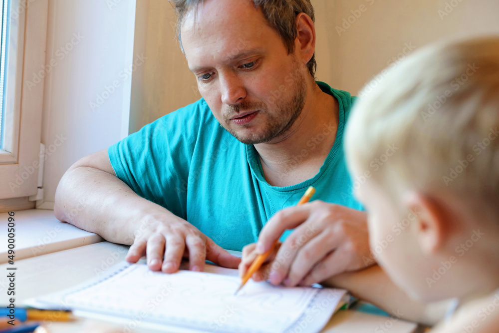 Teaching a child to write. Calligraphy in writing. An adult works with a child. Teaching a child to write. Calligraphy in writing. An adult works with a child.