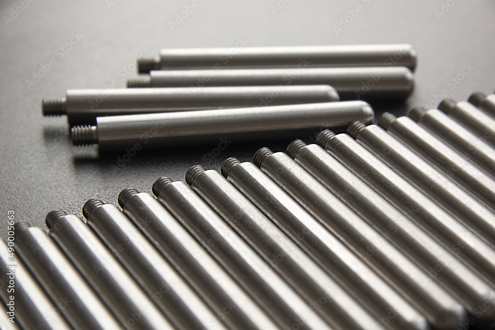Stainless steel turning parts with thread lie in a row on the table on a black background. Factory, metal processing plant. Stainless steel turning parts with thread lie in a row on the table on a black background. Factory, metal processing plant.