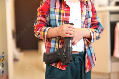 The child is holding a weapon. A gun in the hands of a boy, danger to life
