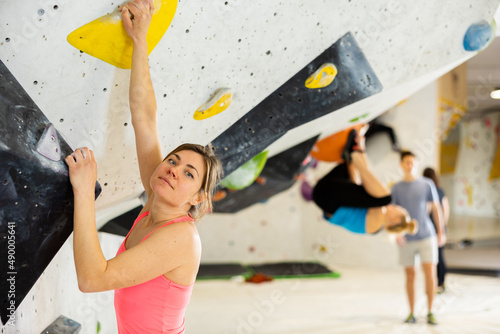 European woman grabbing ledges of artificial climbing wall in bouldering centre.