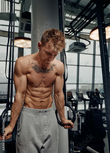 Strong man doing exercise on to gymnastic rings at gym. Fit male athlete training on gymnastic rings in light sport hall © Georgii