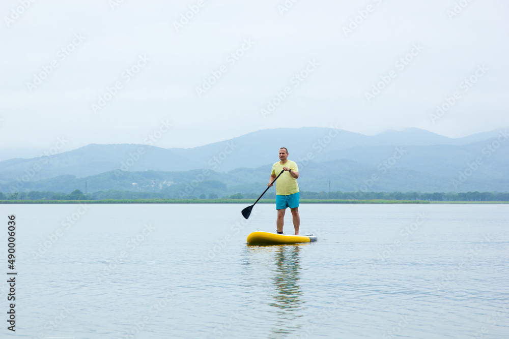 Naklejka premium A young man ride a paddle board on the lake. Supboard water sport activity