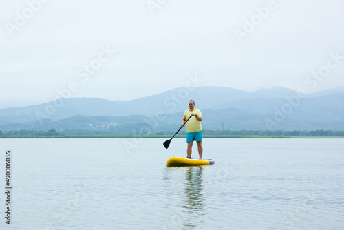 A young man ride a paddle board on the lake. Supboard water sport activity