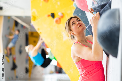 Woman climbing on rock-climbing wall during training in bouldering gym.