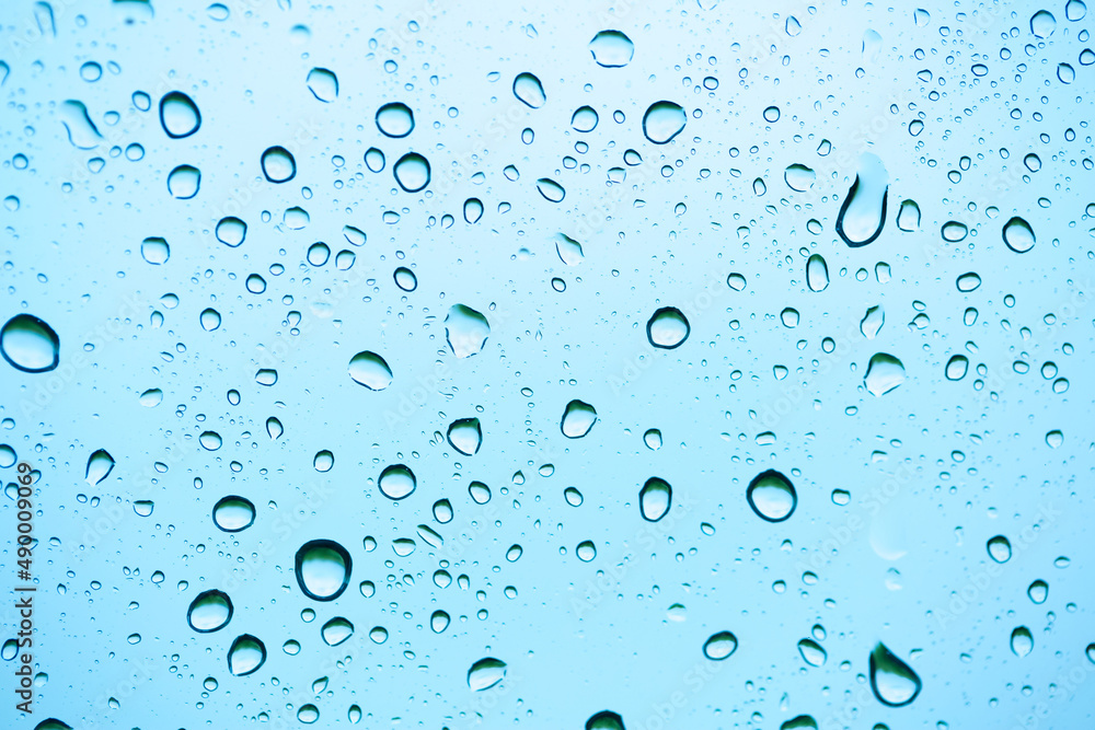 Rain outside the window. Water droplets on a car glass on a background of blue sky and green grass. Overcast. Wet clean nature, ecology