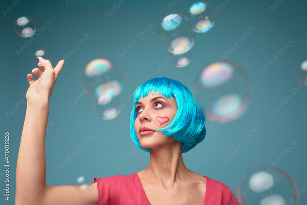 Beautiful young woman with blue wig and bright make-up in soap bubbles. Fashion model girl with creative color makeup. Women doll concept. Beautiful young woman with blue wig and bright make-up in soap bubbles. Fashion model girl with creative color makeup. Women doll concept.