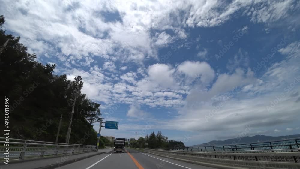 OKINAWA, JAPAN - AUGUST 2021 : Driving shot of Okinawa in daytime. Wide camera, point of view, seaside road drive. Blue sunny sky. Summer holiday, vacation and adventure journey travel concept video. OKINAWA, JAPAN - AUGUST 2021 : Driving shot of Okinawa in daytime. Wide camera, point of view, seaside road drive. Blue sunny sky. Summer holiday, vacation and adventure journey travel concept video.