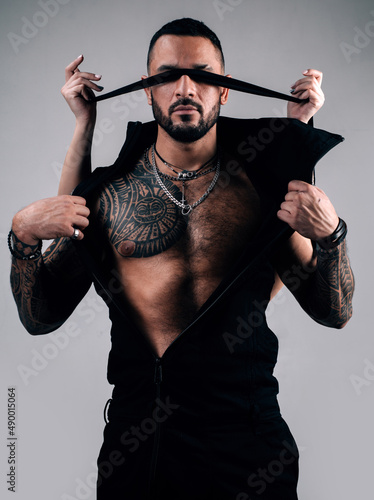Portrait of handsome man with ribbon on eyes. Trust concept. Muscular macho man with athletic body. Female hands cover male eyes with rope.