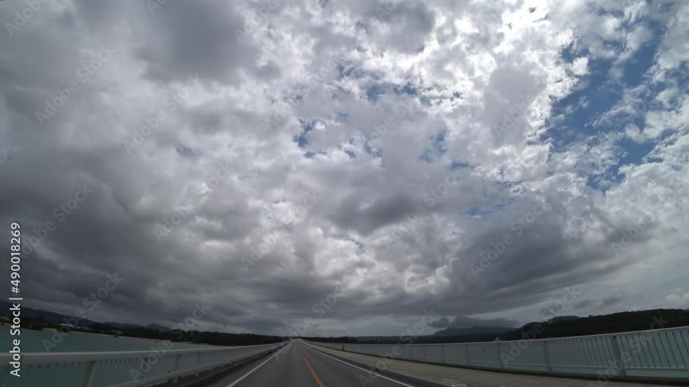 OKINAWA, JAPAN - AUG 2021 : Driving around Kouri Island bridge in sunny summer day. Wide camera, point of view (POV), seaside road driving. Holiday, vacation and resort concept. OKINAWA, JAPAN - AUG 2021 : Driving around Kouri Island bridge in sunny summer day. Wide camera, point of view (POV), seaside road driving. Holiday, vacation and resort concept.