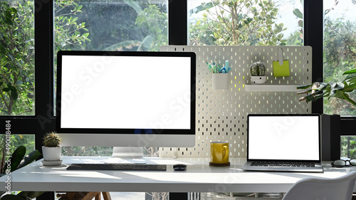 Mockup computer pc, laptop, houseplant and supplies on white table at modern workplace. Blank screen for advertisement.
