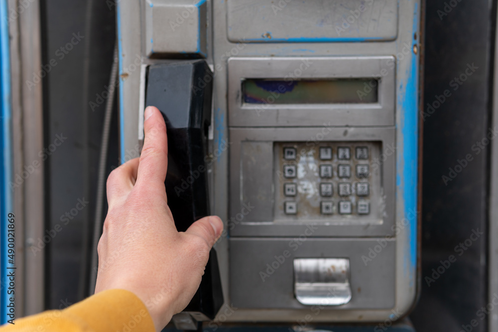 A hand holding a phone in an old booth. Hand of a young man picking up the phone in a call made from an old Spanish phone booth from the 90s. A hand holding a phone in an old booth. Hand of a young man picking up the phone in a call made from an old Spanish phone booth from the 90s.