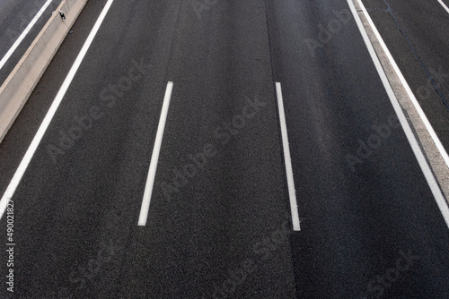 Road background composed of several lanes in an abstract way. Dark three lane highway with white lines.