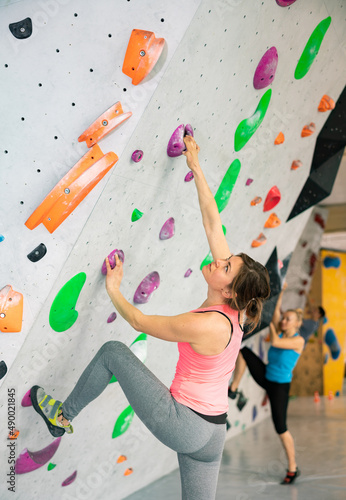 European woman grabbing ledges of artificial climbing wall in bouldering centre.