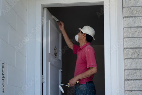 Man wearing facemask, painting a white door with paintbrush.