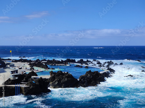 Natural pools in the middle of the Atlantic ocean in Madeira Island, Portugal. Amazing holiday times. Clouds with sun. Ocean and waves hitting the rocks. People in the water.