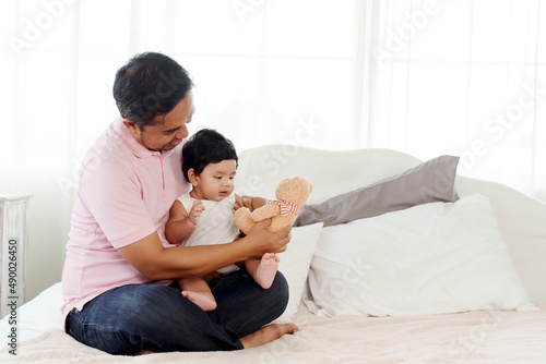 The joys of an Asian dad family are bottle feeding their 4-month-old baby happily and warmly in bed in their bedroom in the morning. happy family concept