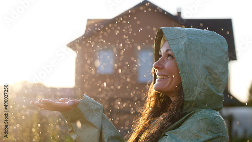 Young happy woman wearing green raincoat is feeling free and smiling under the rain. Concept of life, freedom, nature, adventure, purity.
