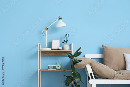 Comfortable sofa, houseplants and modern lamp on table near blue wall