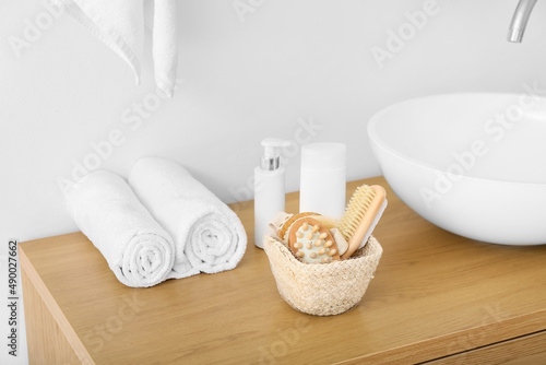Basket with massage body brushes and bath supplies on table near sink in bathroom