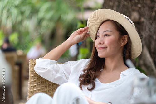 Portrait image of a beautiful young asian woman in white shirt with hat sitting and relaxing in the park © Farknot Architect