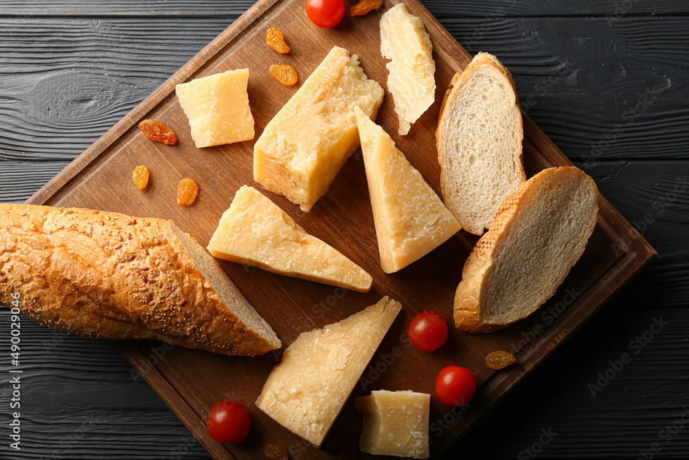 Fototapeta premium Board with pieces of tasty Parmesan cheese and bread on black wooden background