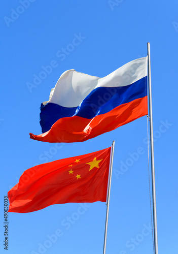 Flags of Russia and China are flying in the wind against the blue sky photo
