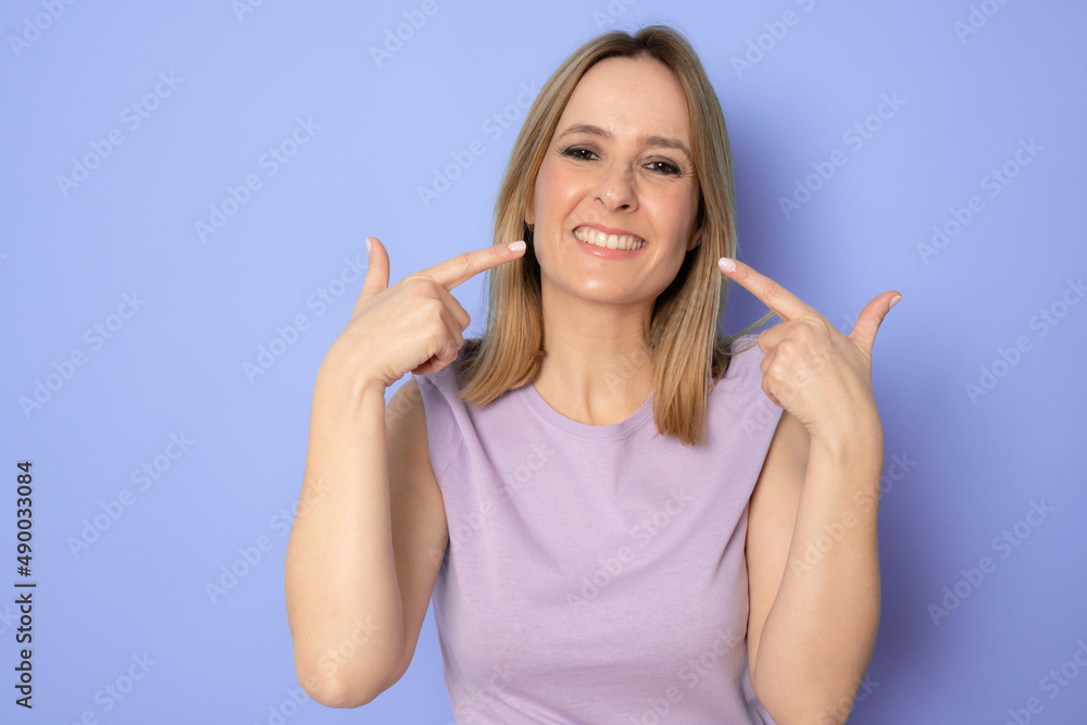 Portrait of smiling woman pointing at her nice teeth and mouth isolated on purple background. Dental concept. Portrait of smiling woman pointing at her nice teeth and mouth isolated on purple background. Dental concept.